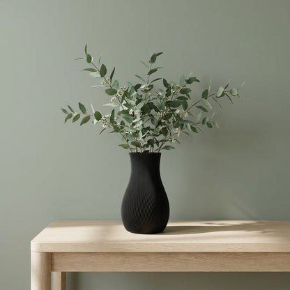 Sort LUMA-vase med grønne grene på et træbord